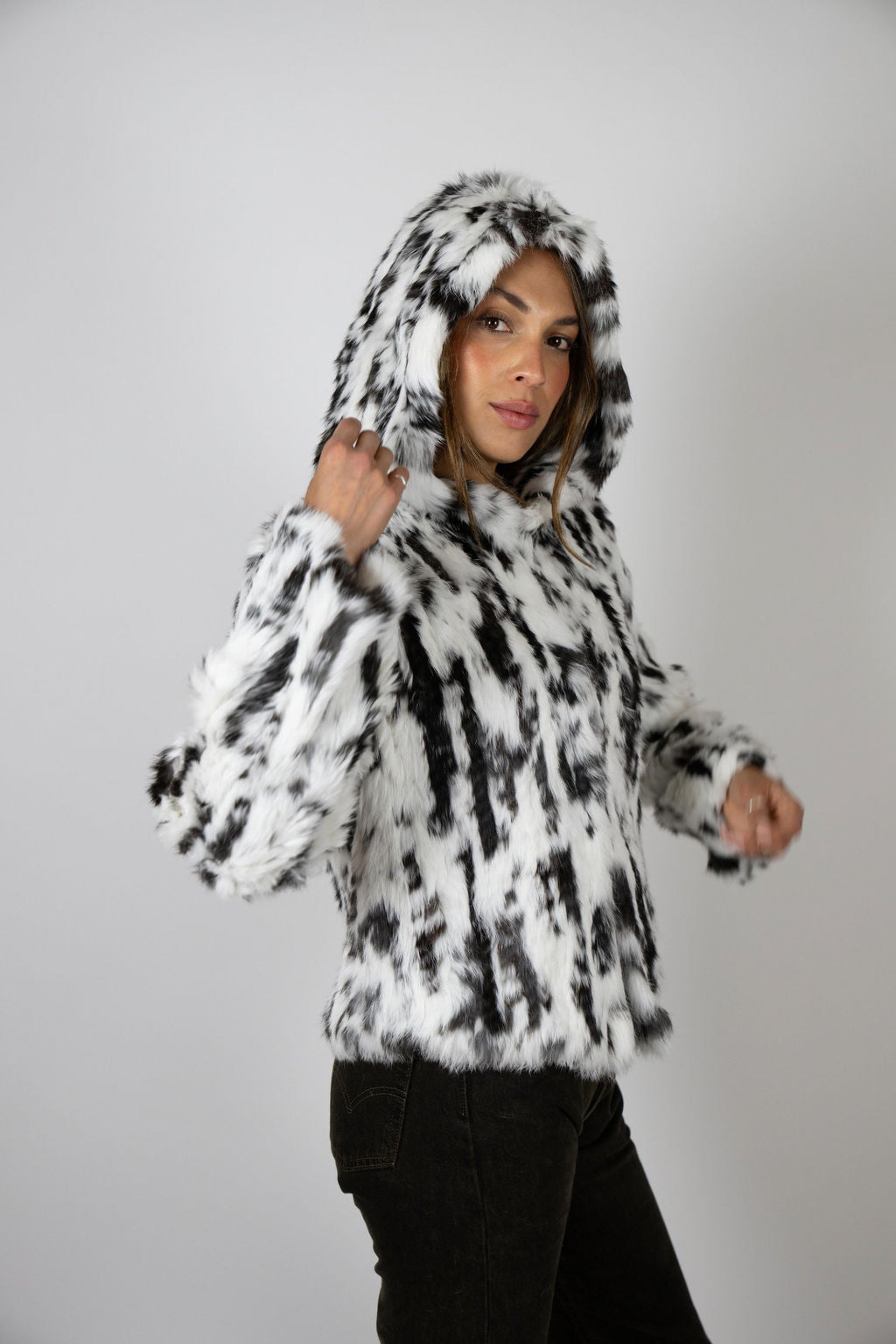 Woman in snow leopard print cropped rabbit fur jacket with hood up, angled side view.