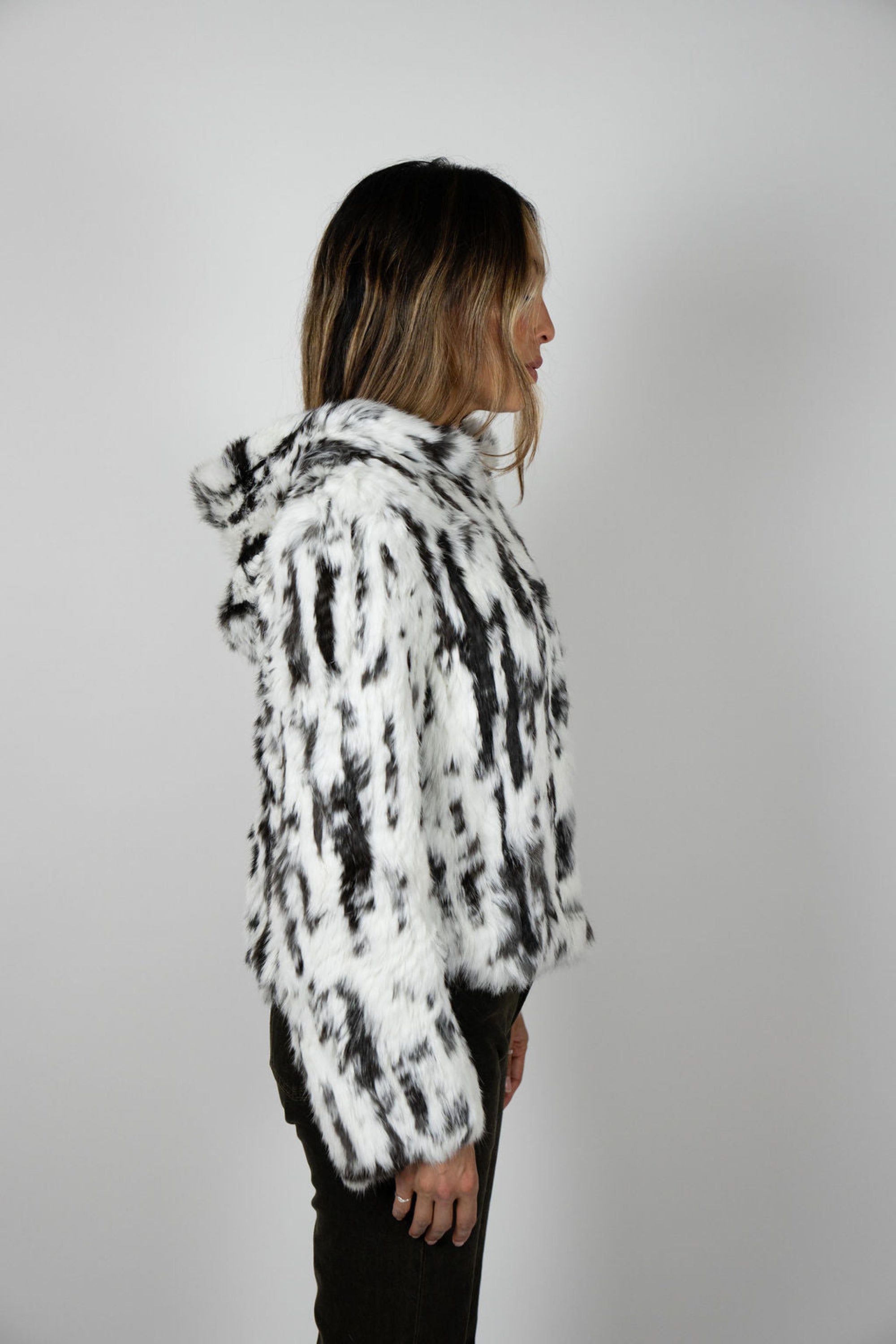 Side profile of cropped black and white fur hooded jacket on model with hands in pockets.
