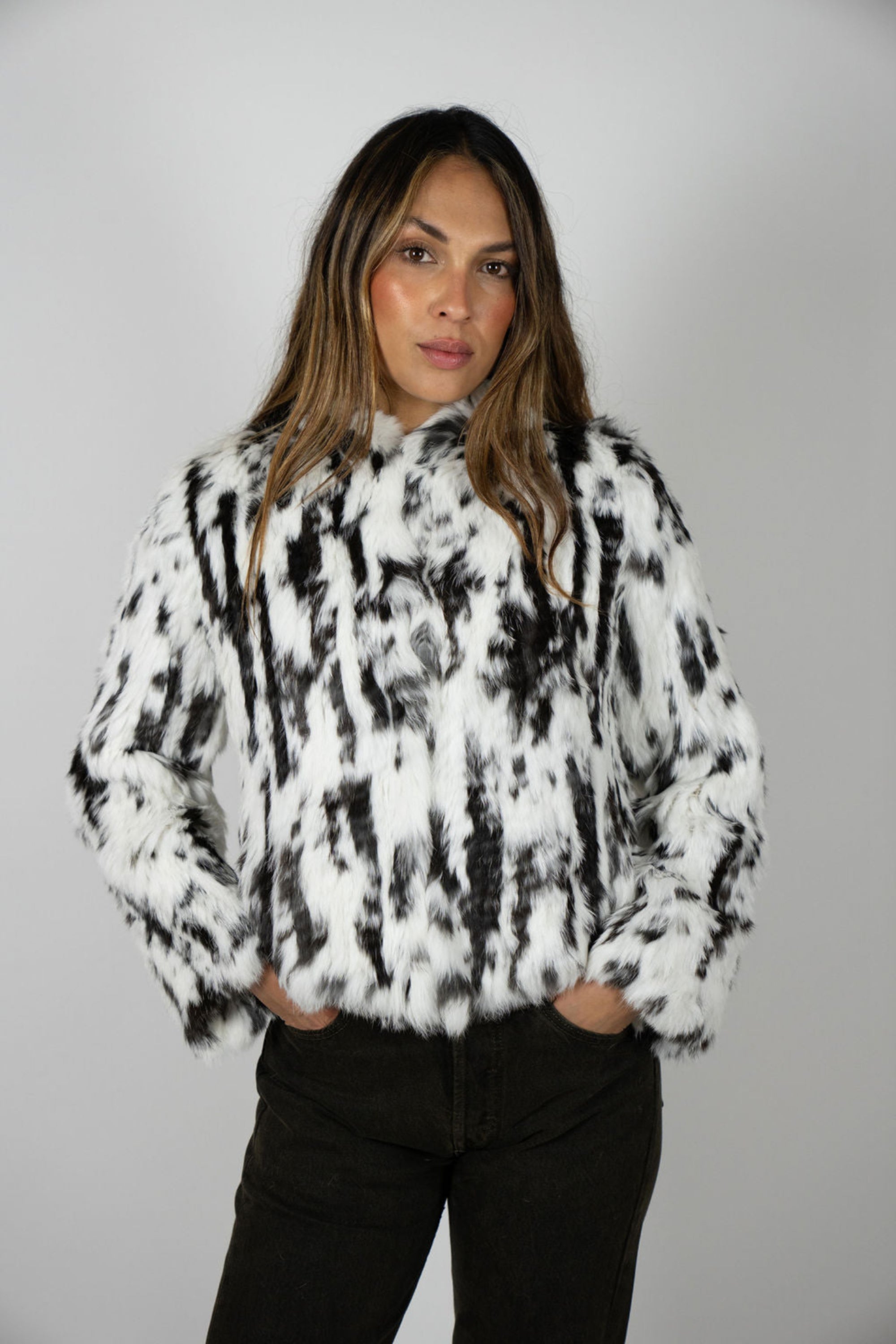 Woman wearing cropped two-tone rabbit fur hooded jacket in snow leopard print, front view.