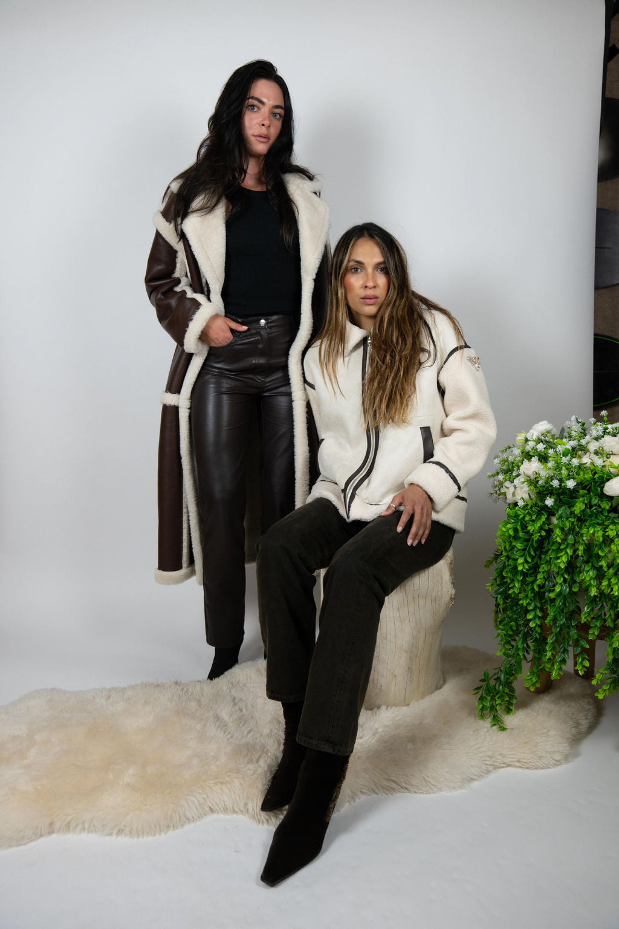 Two women in Angel Wings winter jackets, featuring the Vandetta Jacket seated with legs crossed