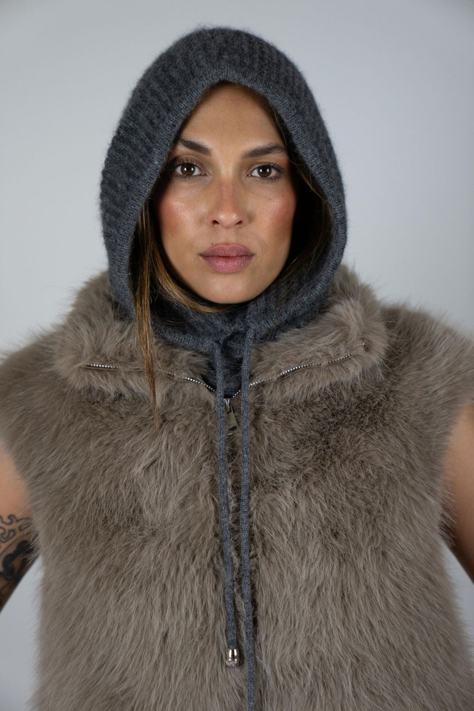 Model wearing the Chalet Knit Hood in Charcoal by Angel Wings by Lucy, styled with a faux fur vest for elevated winter and luxury resort layering.