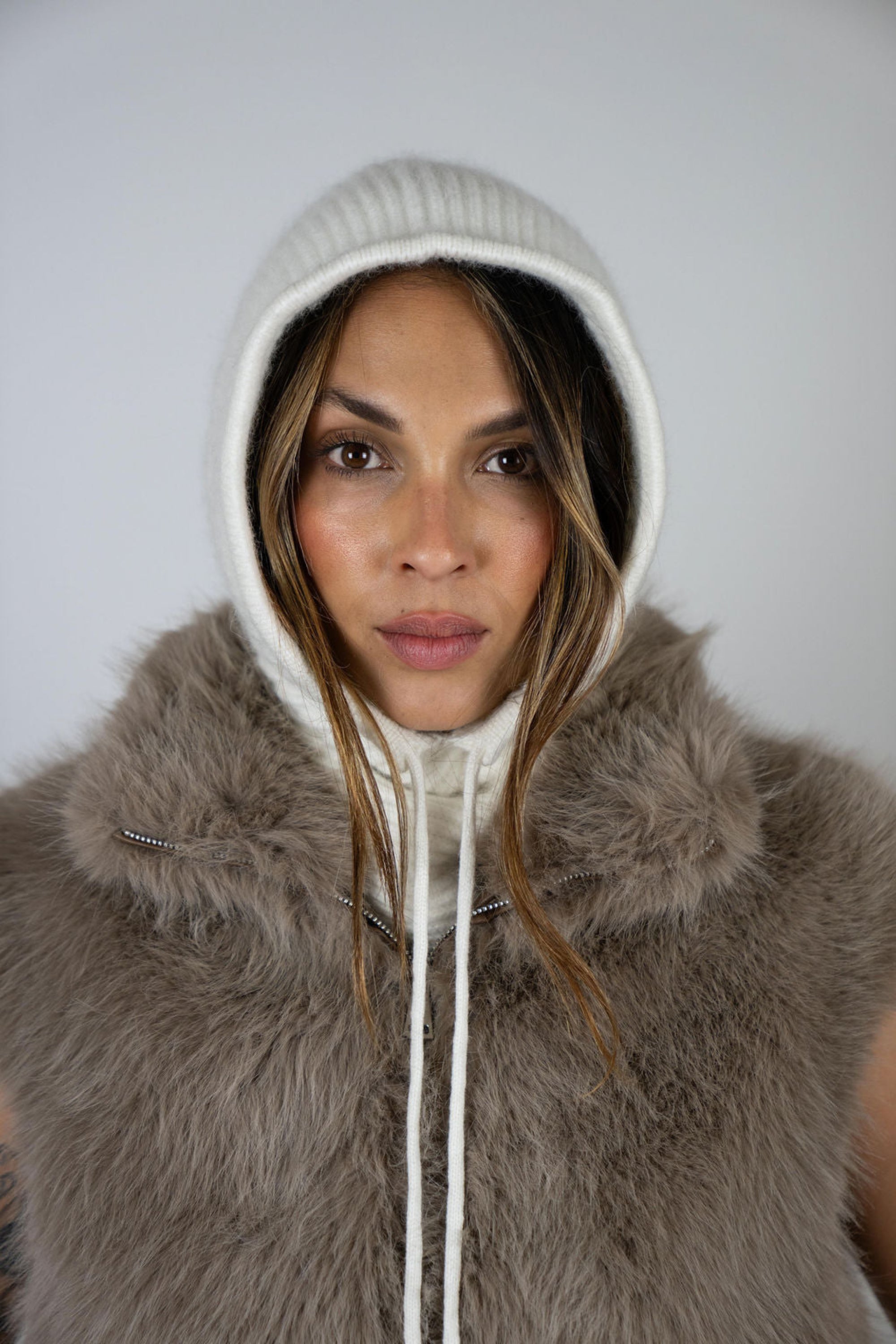 Model wearing the Chalet Knit Hood in Snow by Angel Wings by Lucy, styled under a faux fur vest for elevated winter resort layering.