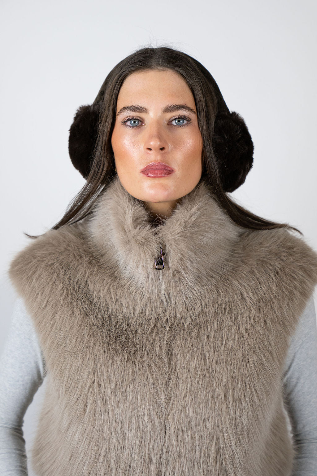 Model wearing faux fur earmuffs in Chocolate by Angel Wings by Lucy, styled with a faux fur vest for elevated winter accessorising.