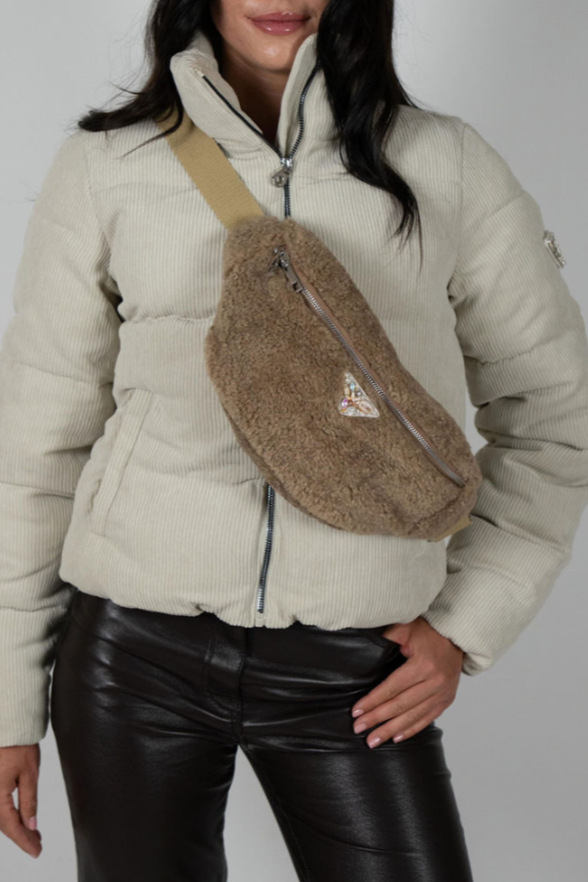 Beige faux shearling crossbody bag with zip closure and triangle emblem worn over cream puffer jacket – Alpine Crossbody by Angel Wings by Lucy