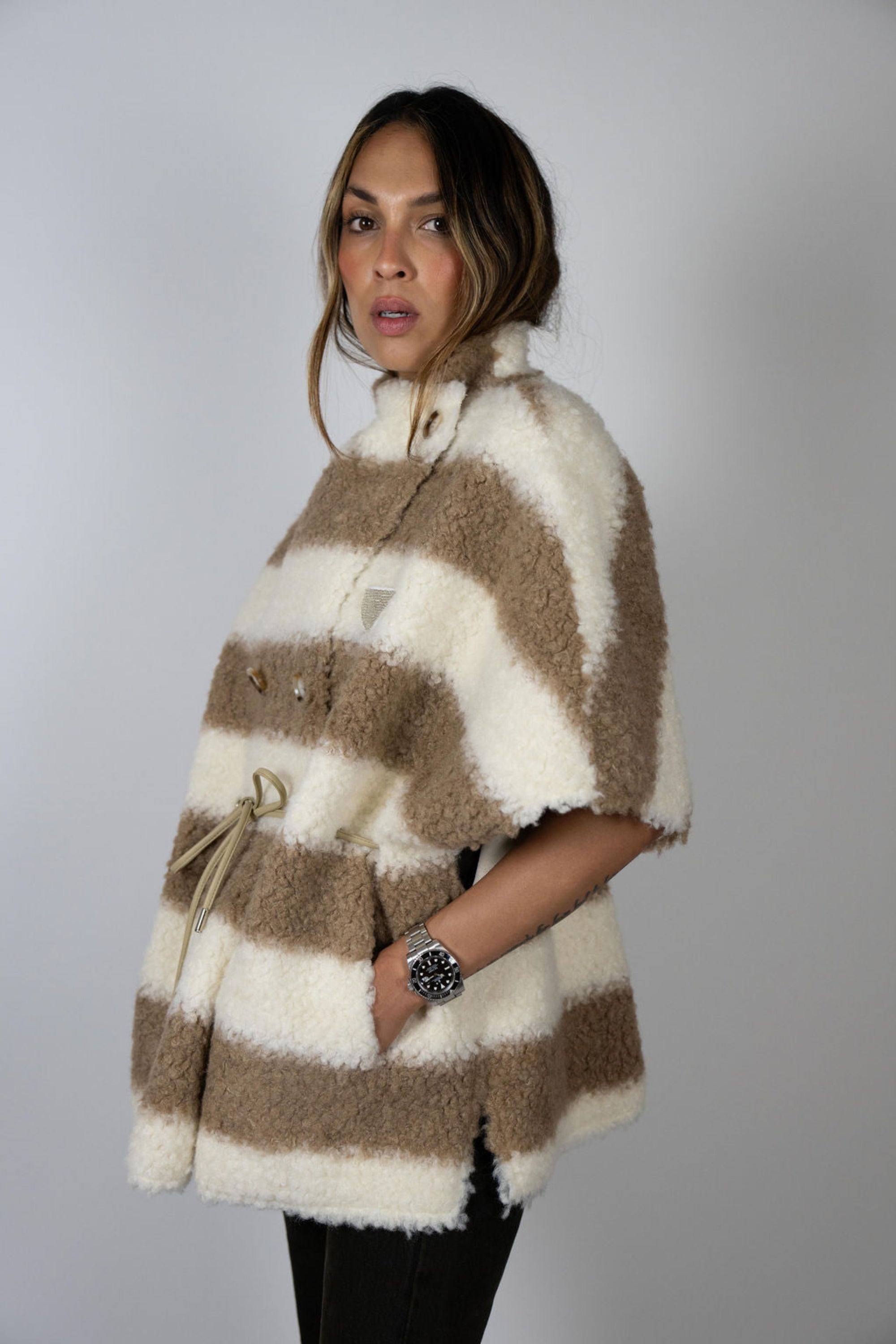 Angel Wings by Lucy wool cape in beige and ivory stripe, oversized with short sleeves, drawstring waist, and buttons, shown on model from side