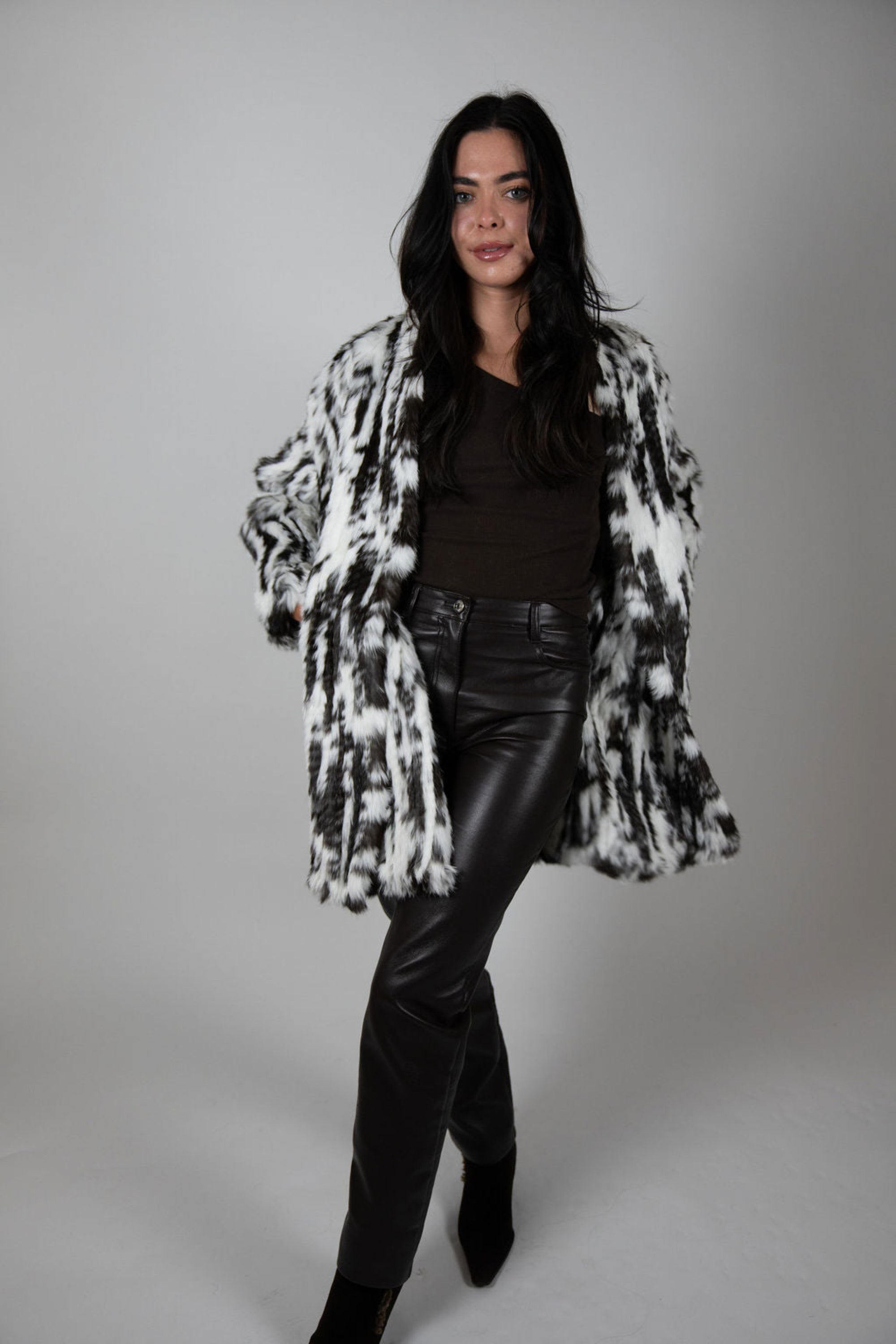 Model wearing snow leopard print faux fur coat, standing with legs crossed.