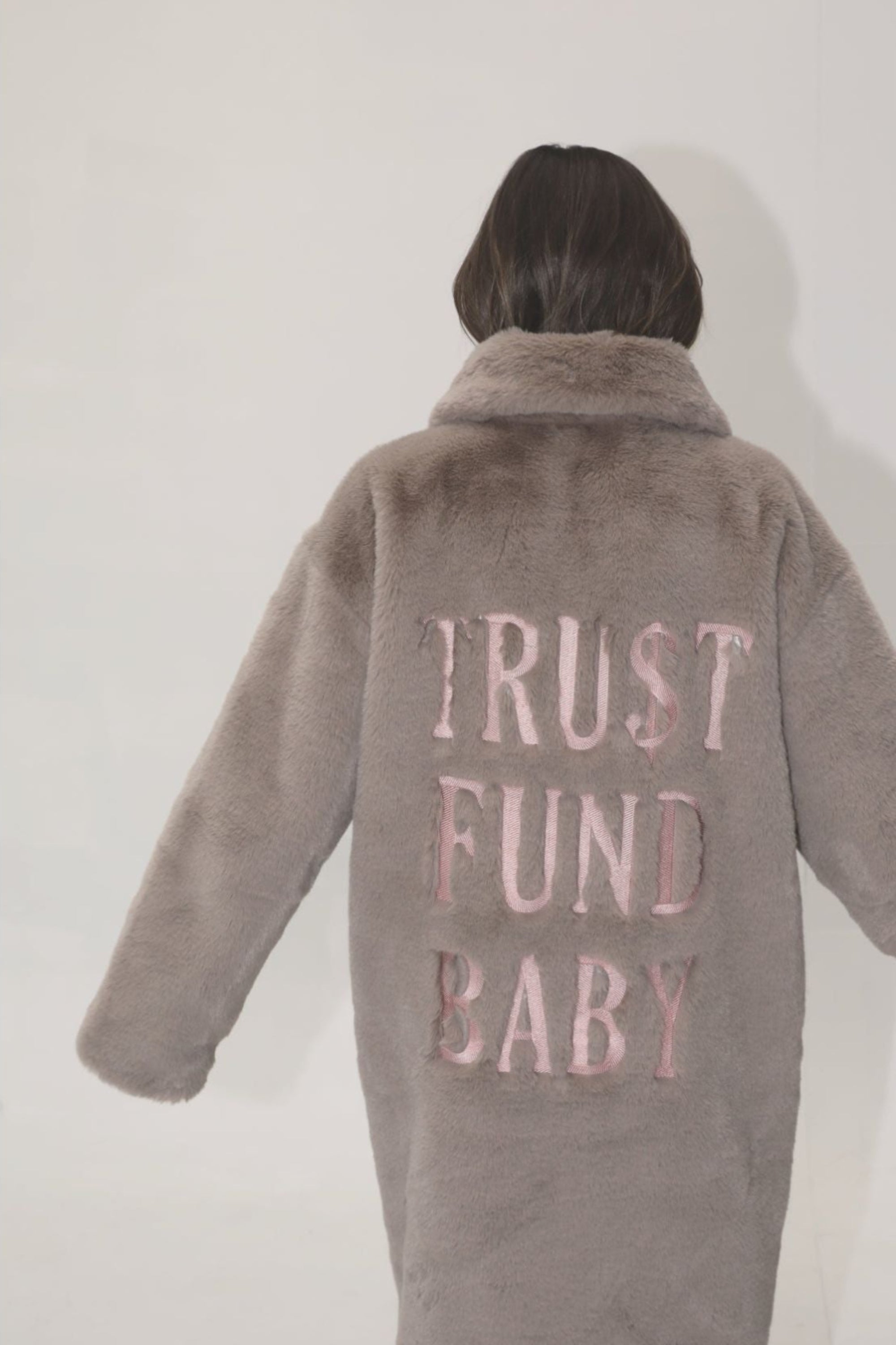 Back view of taupe faux fur jacket with light pink “TRU$T FUND BABY” lettering — from the Mr. Greys statement collection.