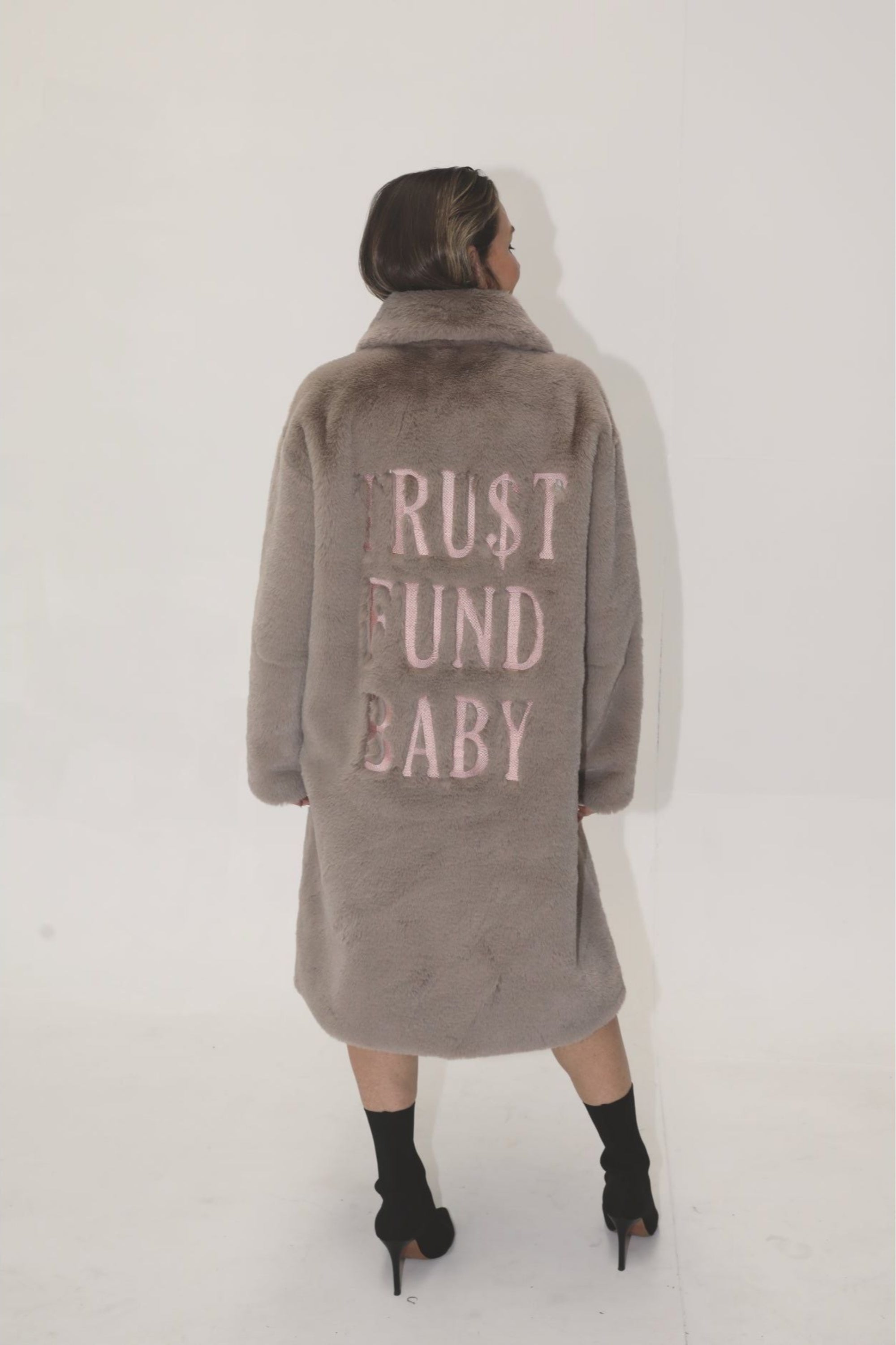 Back view of taupe faux fur jacket with light pink “TRU$T FUND BABY” lettering — from the Mr. Greys statement collection.