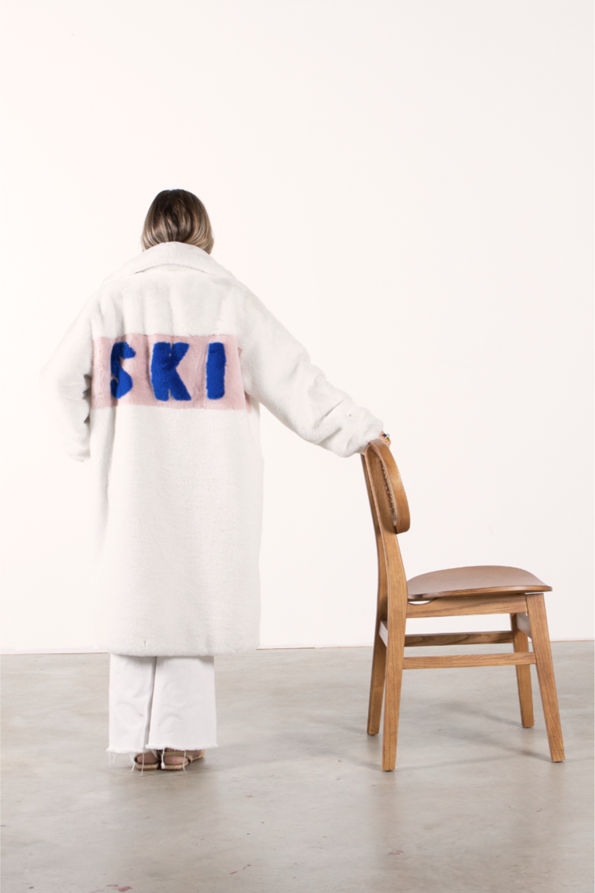 Back view of white faux fur jacket with blush panel and bold cobalt blue “SKI” lettering — part of the Mr. Greys collection.