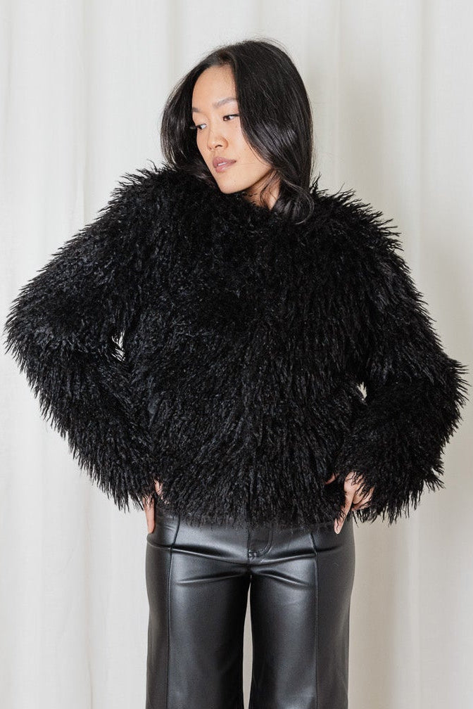 Model wearing the Angel Wings Yeti Jacket in Black, a shaggy faux-fur jacket styled with black leather pants and boots.