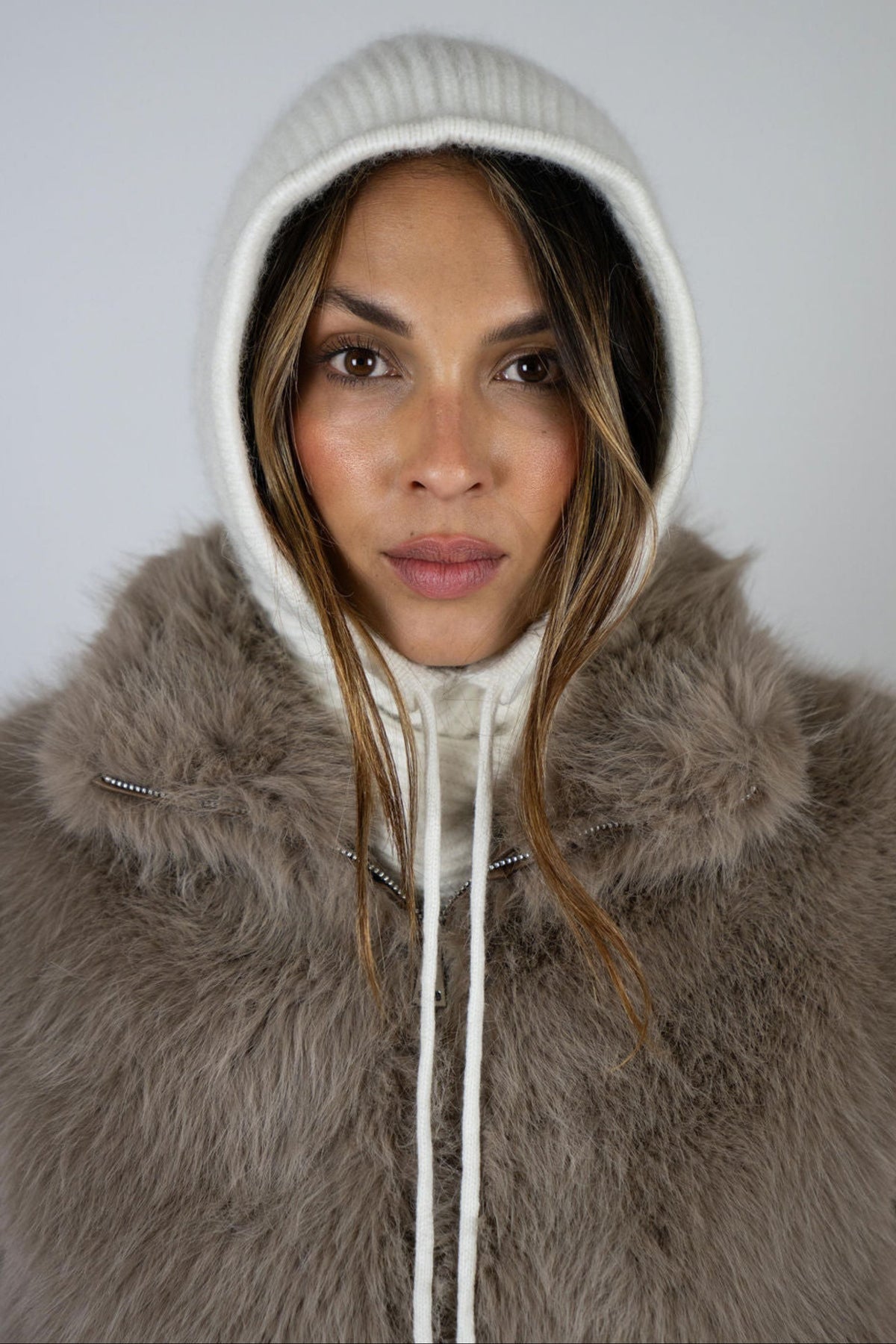 Model wearing the Chalet Knit Hood in Snow by Angel Wings by Lucy, styled under a faux fur vest for elevated winter resort layering.