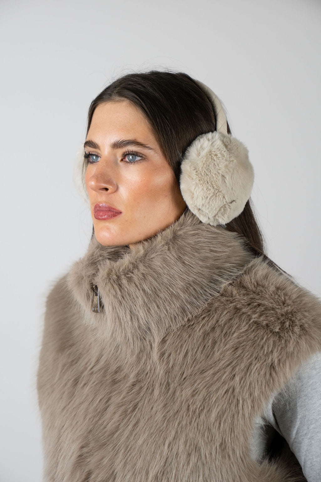 Model wearing faux fur earmuffs in Beige by Angel Wings by Lucy, styled with a faux fur vest for elevated winter accessorising.