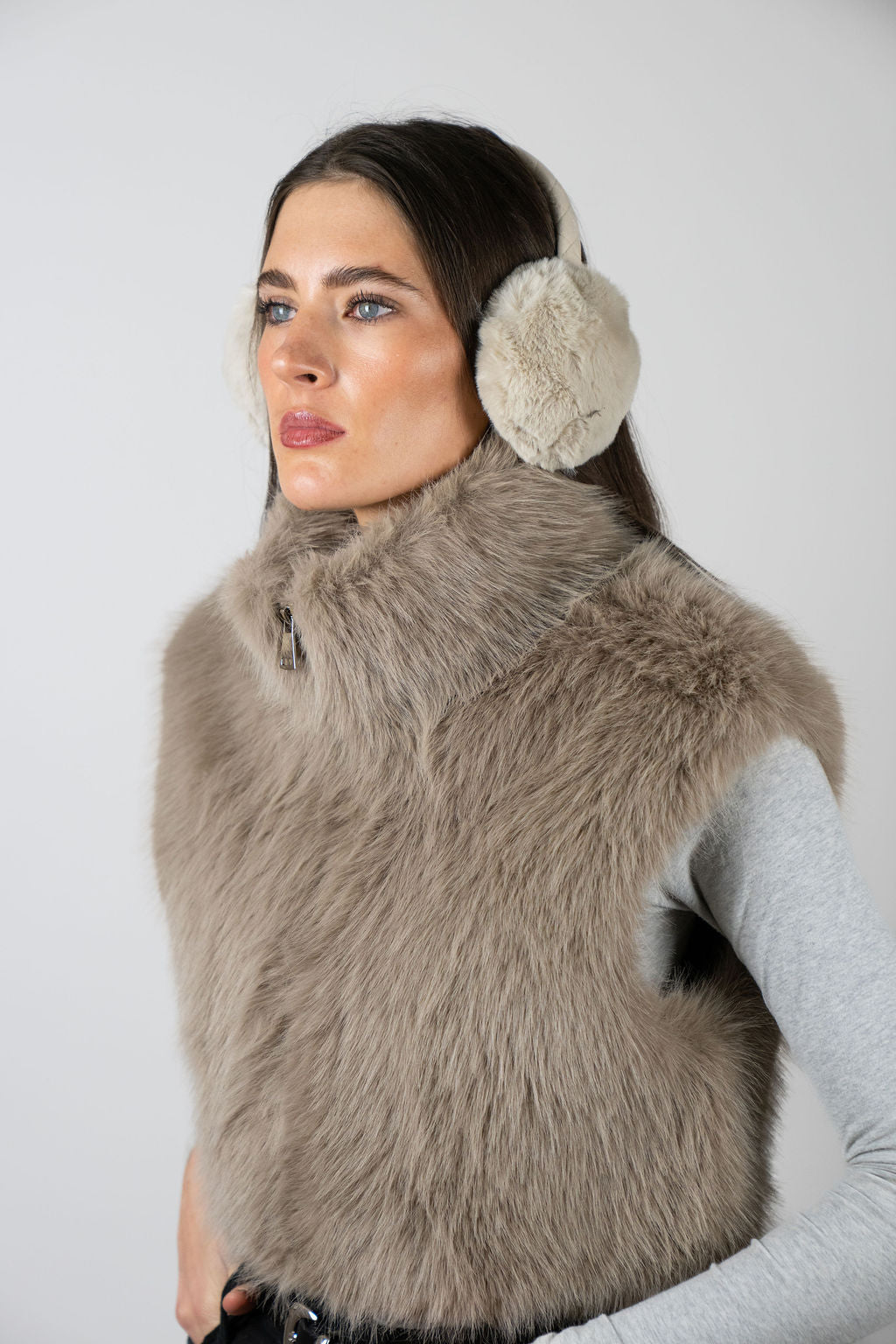 Model wearing faux fur earmuffs in Beige by Angel Wings by Lucy, styled with a faux fur vest for elevated winter accessorising.