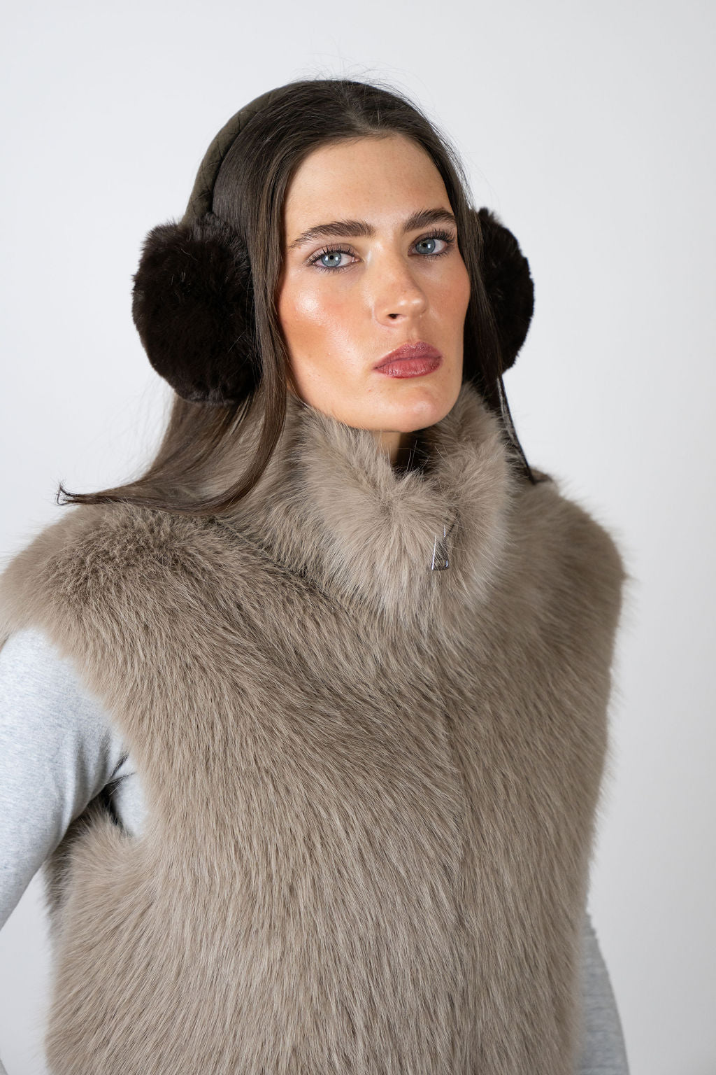 Model wearing faux fur earmuffs in Chocolate by Angel Wings by Lucy, styled with a faux fur vest for elevated winter accessorising.
