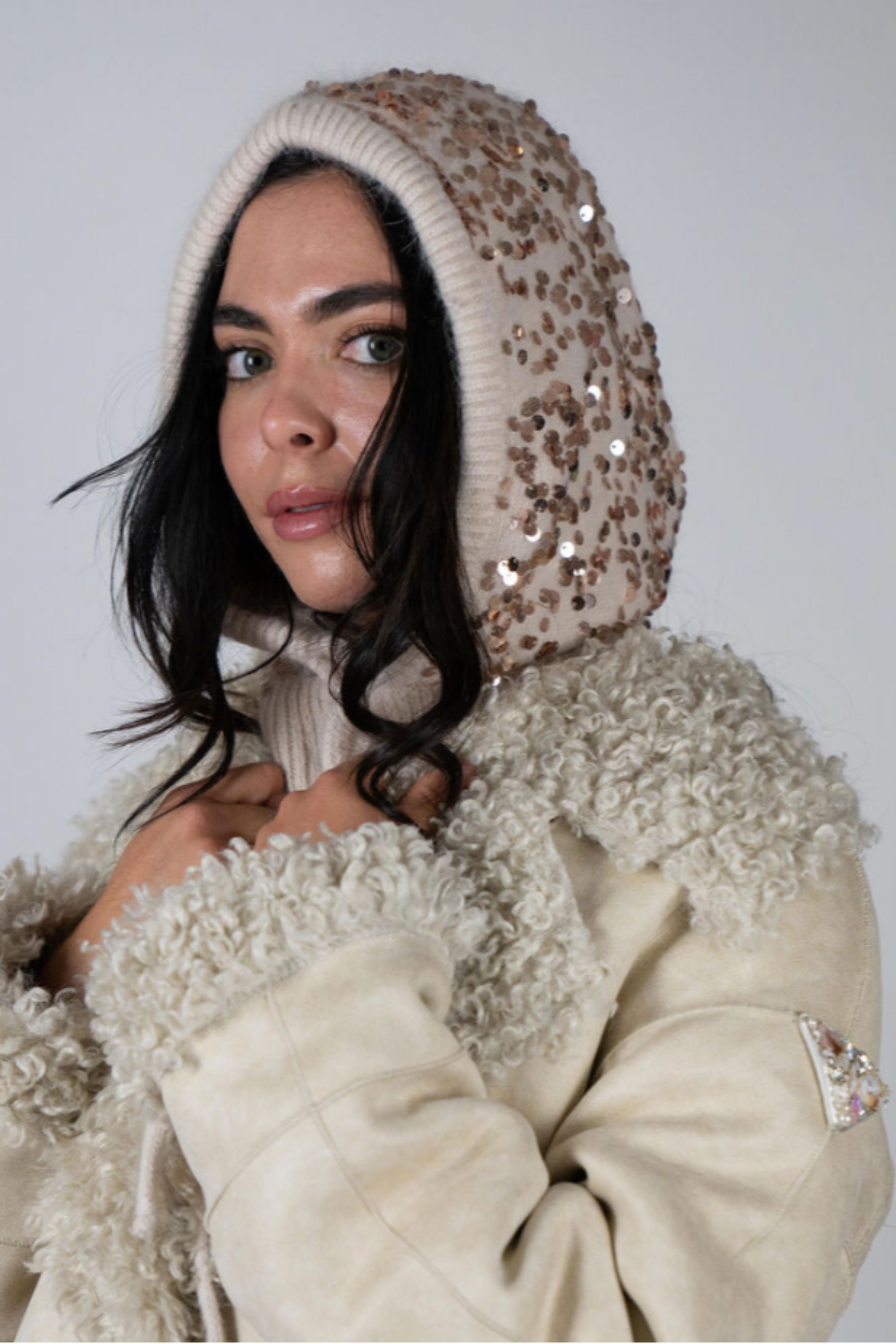 Model wearing the Sequin Knit Hood in Beige by Angel Wings by Lucy, a luxury knit hood with subtle sequin detailing designed for elevated winter and resort styling.