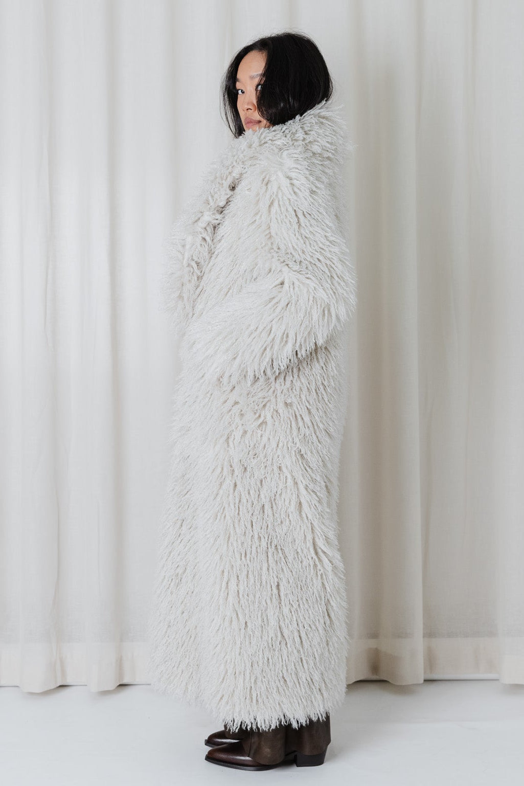Side view of model wearing the Angel Wings Yeti Coat in Snow, a long shaggy faux-fur winter coat.
