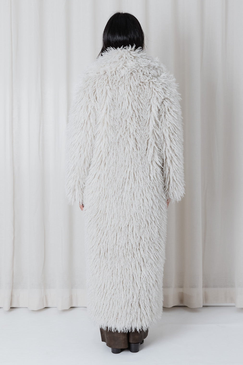 Back view of model wearing the Angel Wings Yeti Coat in Snow, a long shaggy faux-fur winter coat.
