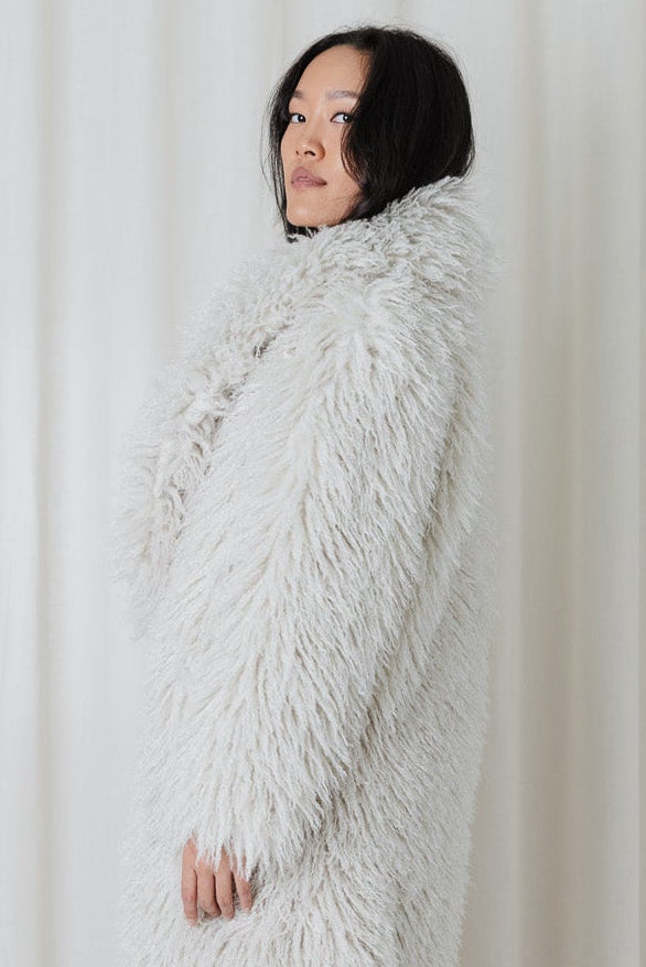 Crop view of model wearing the Angel Wings Yeti Coat in Snow, a long shaggy faux-fur winter coat.
