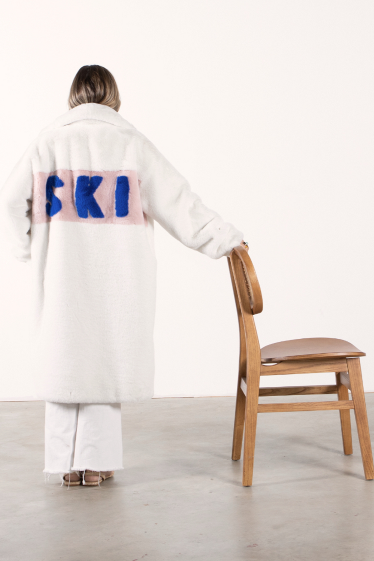 Back view of white faux fur jacket with blush panel and bold cobalt blue “SKI” lettering — part of the Mr. Greys collection.